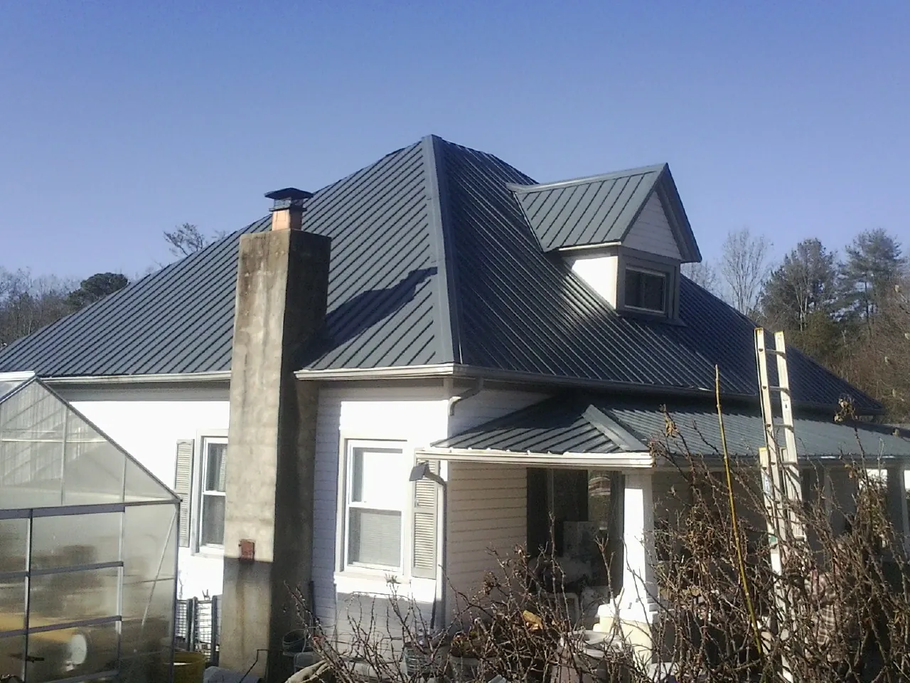 Dark blue standing seam metal roof on a white farmhouse with dormer — Slate & Tile Roof Repair by Roofing Brothers in Saint Augustine