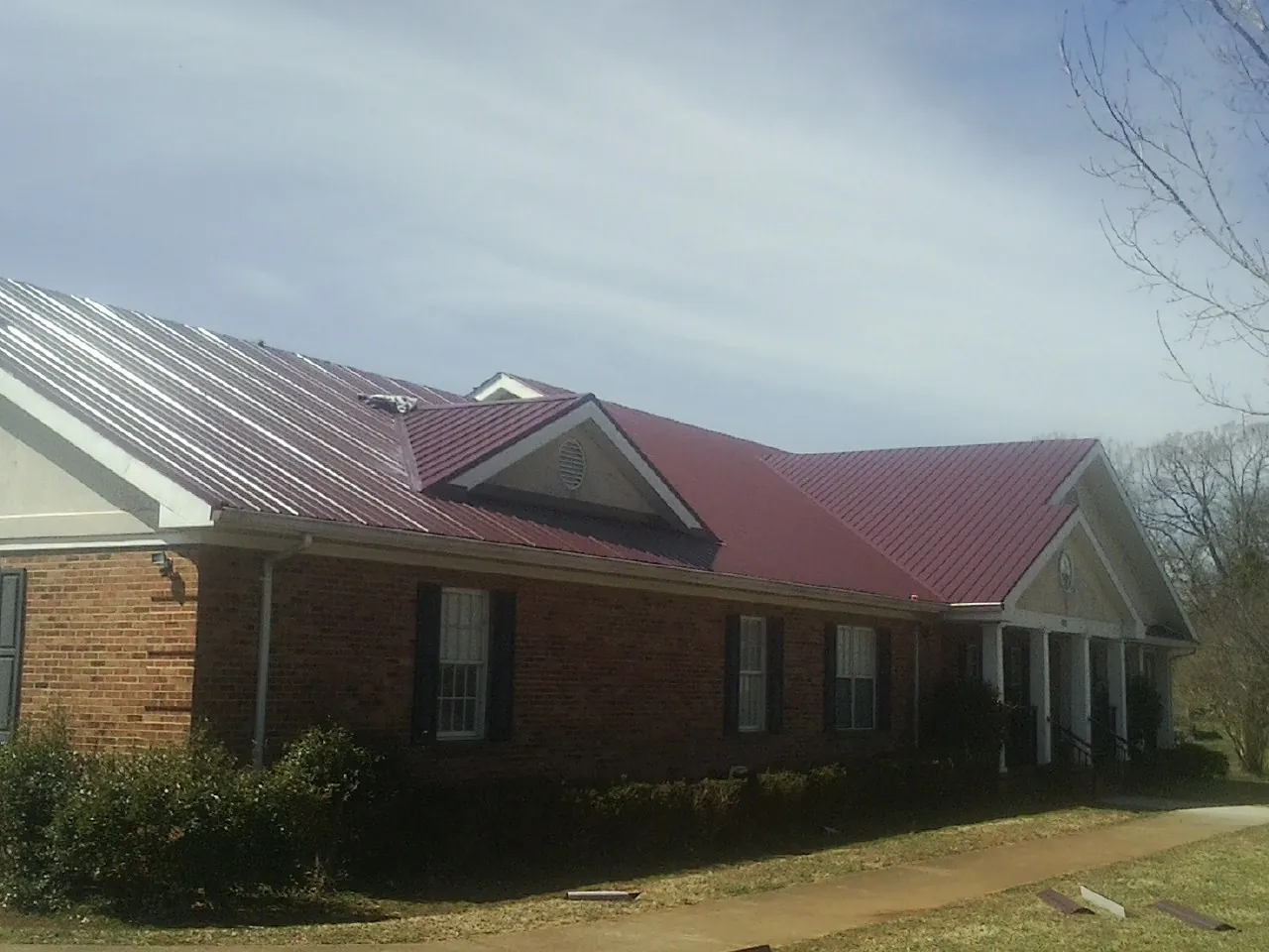 Red metal roof with gabled entries on a long brick building, from a Hail Damage Roof Repair job in Saint Augustine