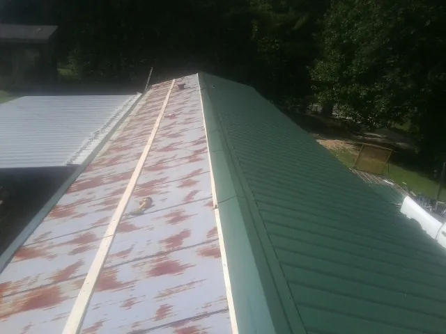 Old rusted panels beside newly installed green metal roofing — Wind Damage Roof Repair by Roofing Brothers in Saint Augustine