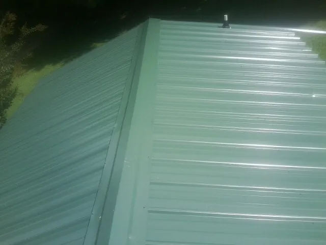 New green metal panels meeting at the ridge of a roof — Flat Roof Repair work by our crew in Saint Augustine