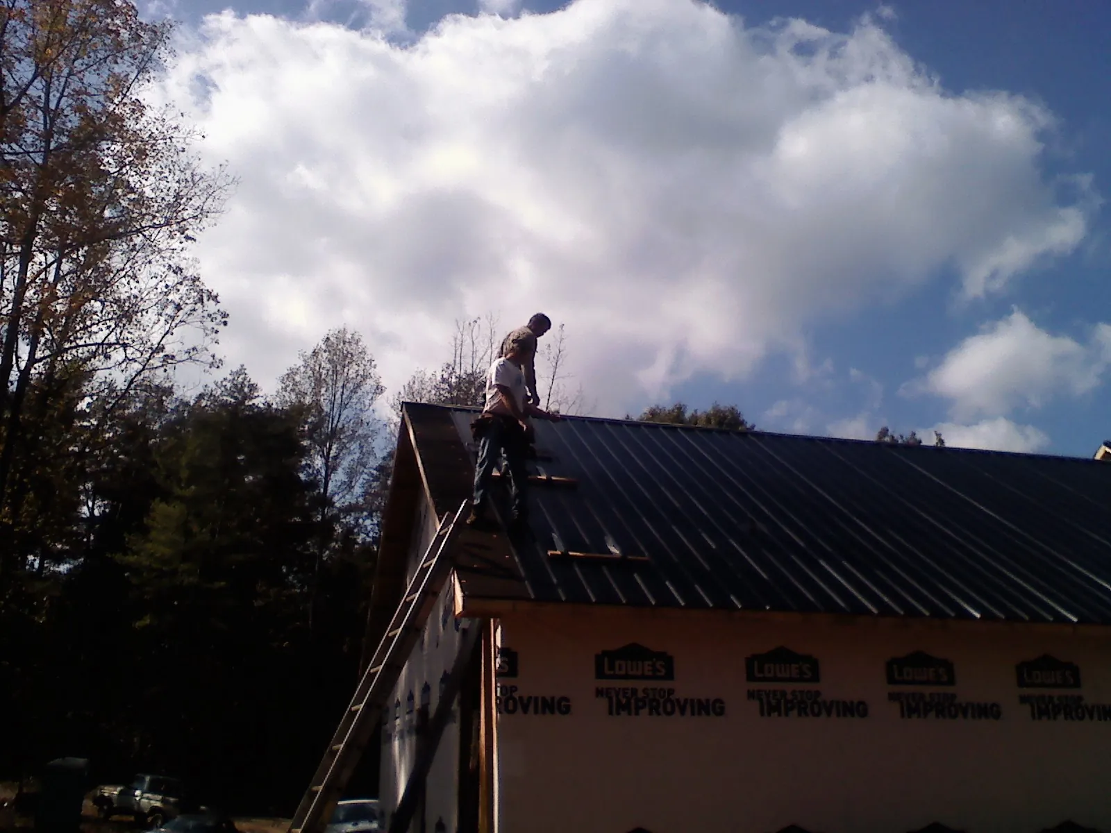 Roofer fastening dark metal panels high against a cloudy sky, from a Roof Inspection job in Saint Augustine