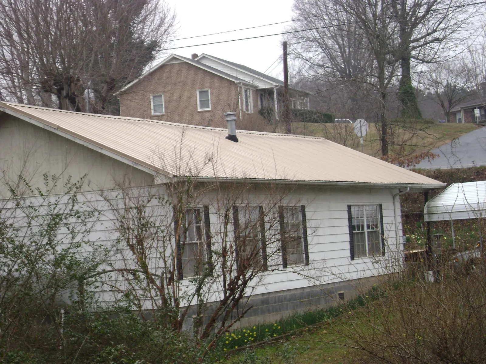 Tan metal roof on a white sided house set into a hillside — Commercial Roofing by Roofing Brothers in Saint Augustine